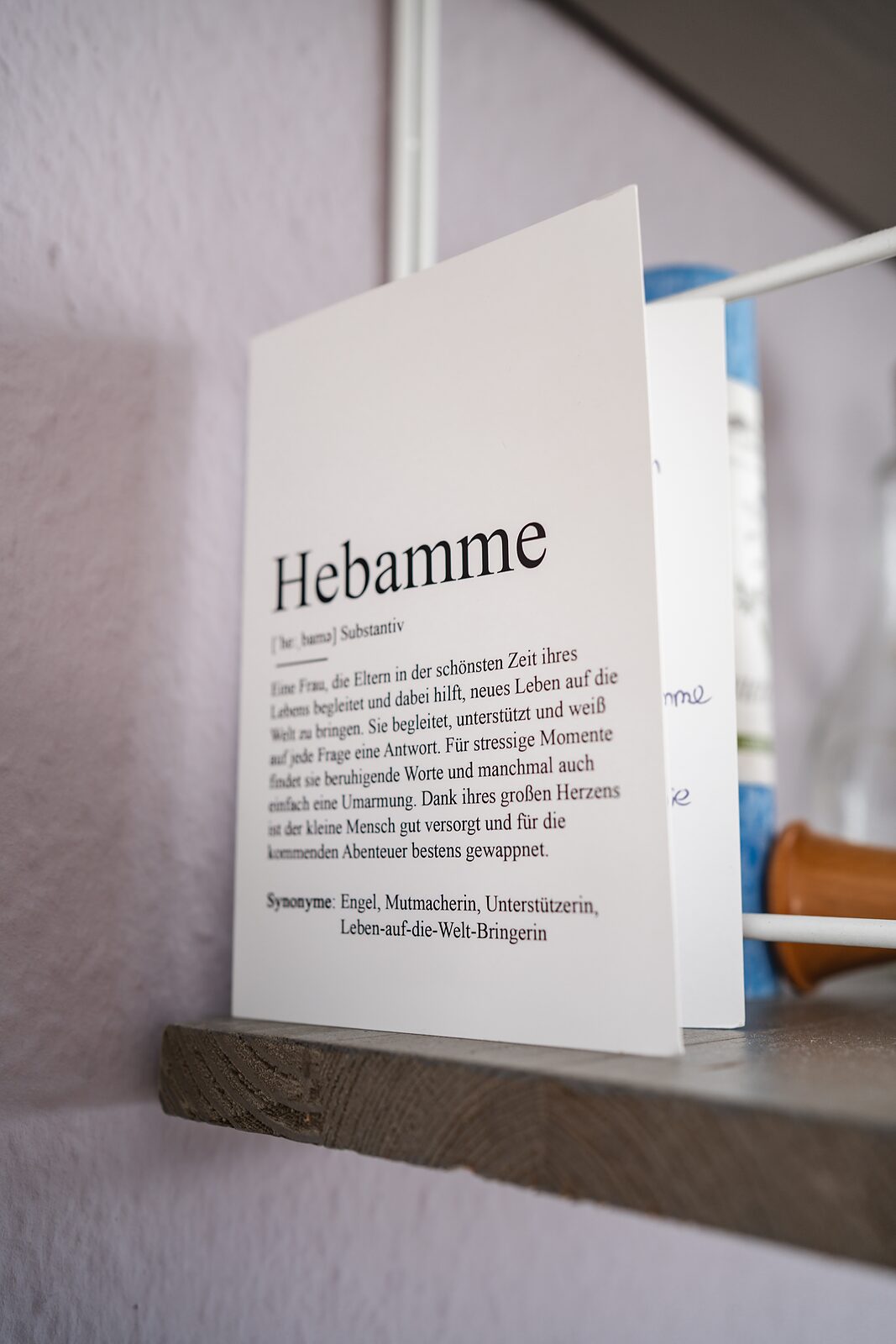 Aufgestellte Karte auf einem Regalbrett mit einer Definition des Wortes Hebamme