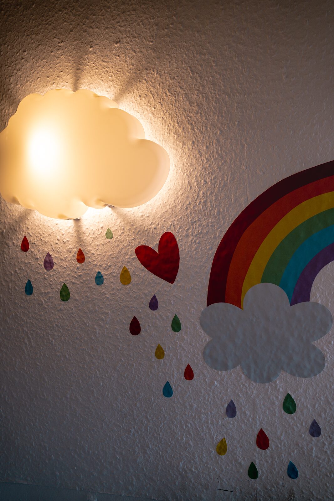 Wandlampe in Wolkenform neben einem gemalten Regenbogen